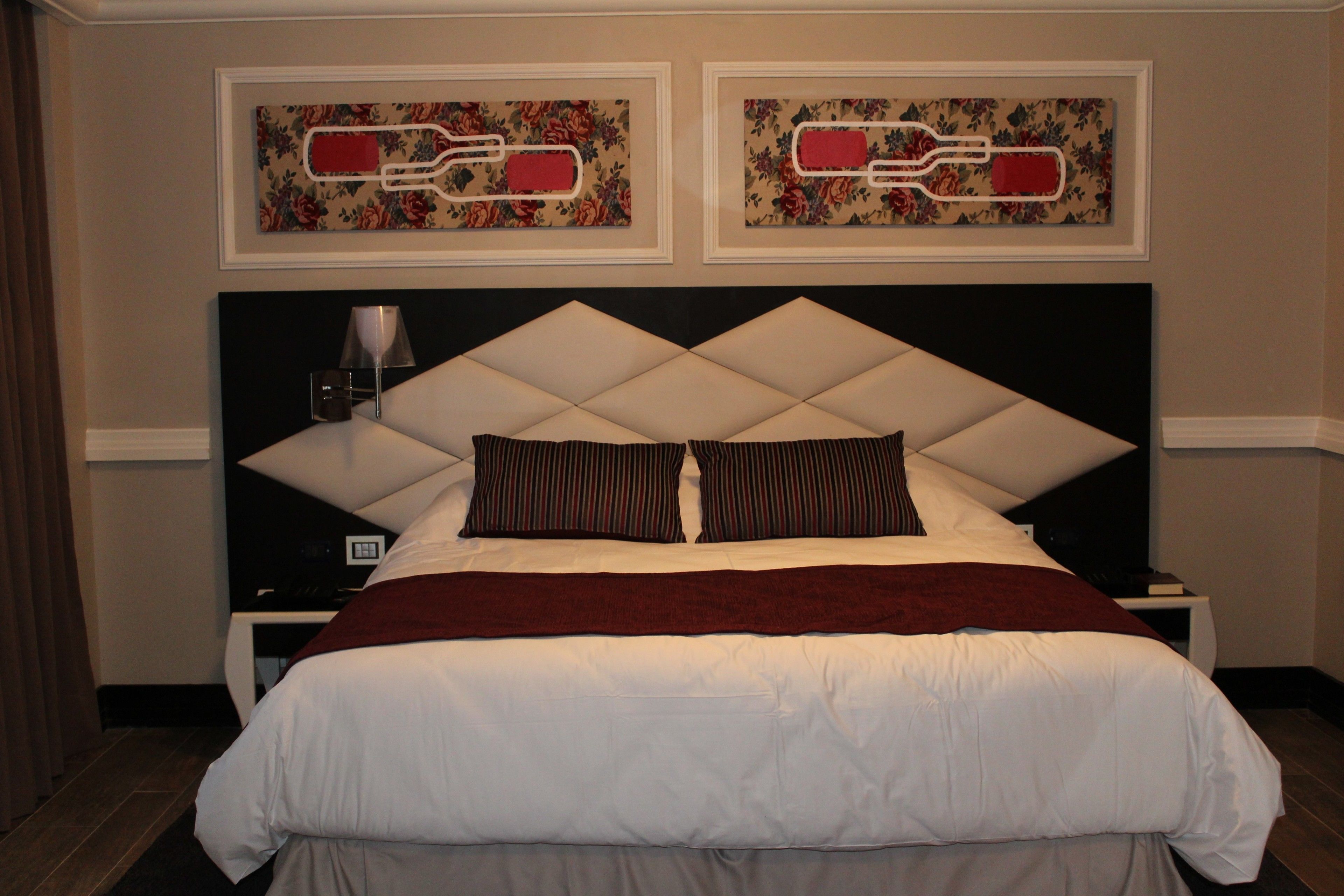 A hotel room with a large bed, two nightstands, a lamp, and two framed floral artworks on the wall.