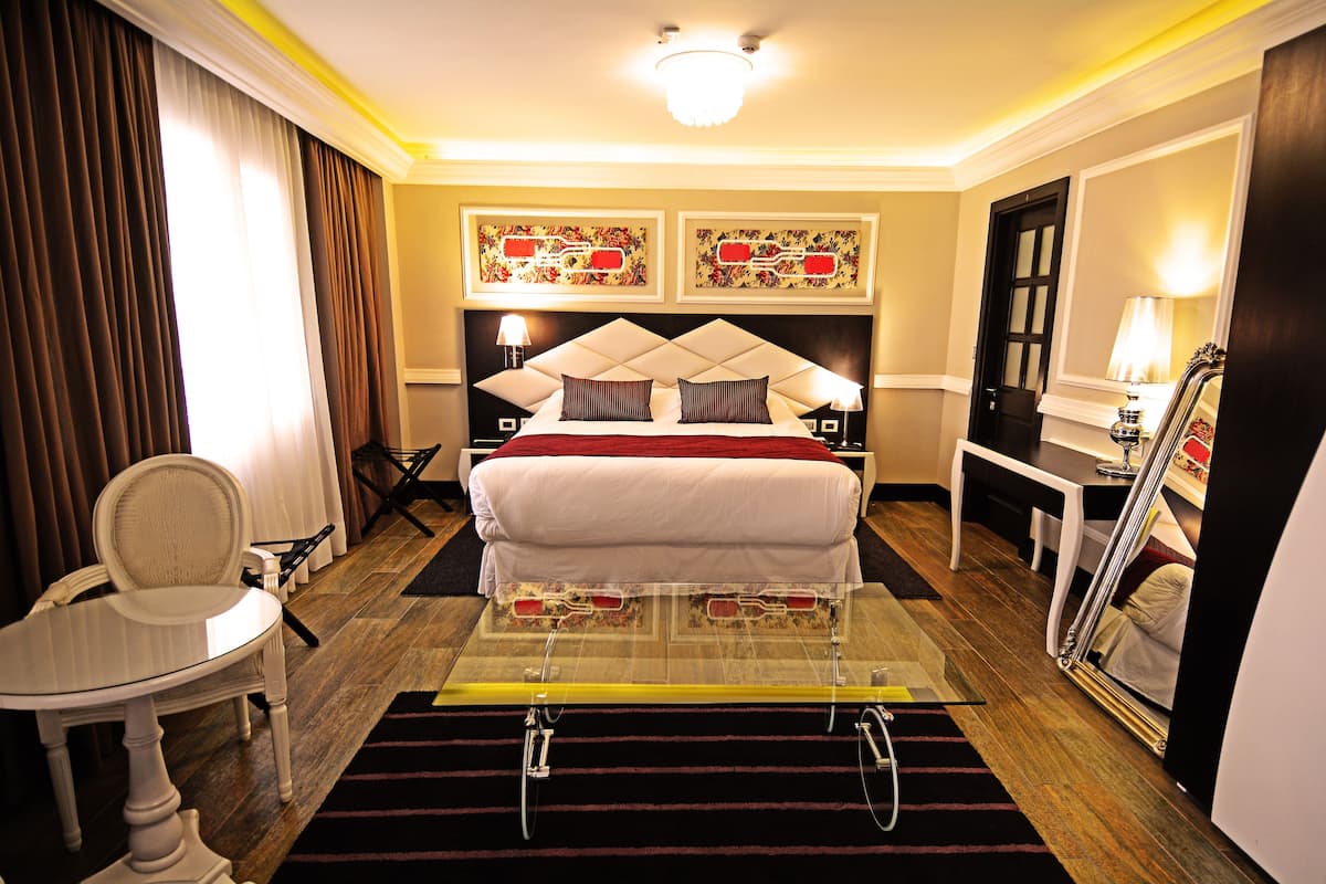 A hotel room with a bed, a desk, a chair, a mirror, and artwork on the walls.