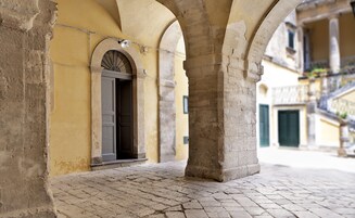 Un patio cubierto con arcos de piedra, una puerta con un vano decorativo y un suelo adoquinado.