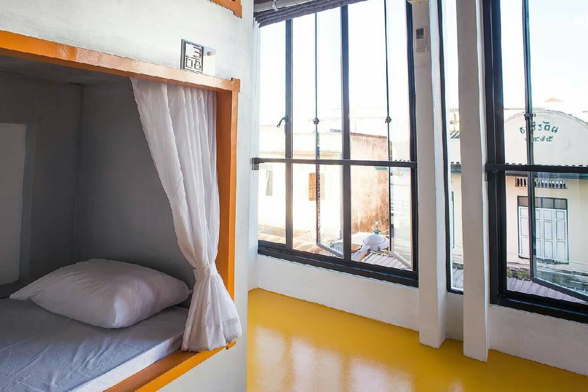 A room with a bunk bed, a window with curtains, and a view of the outside.