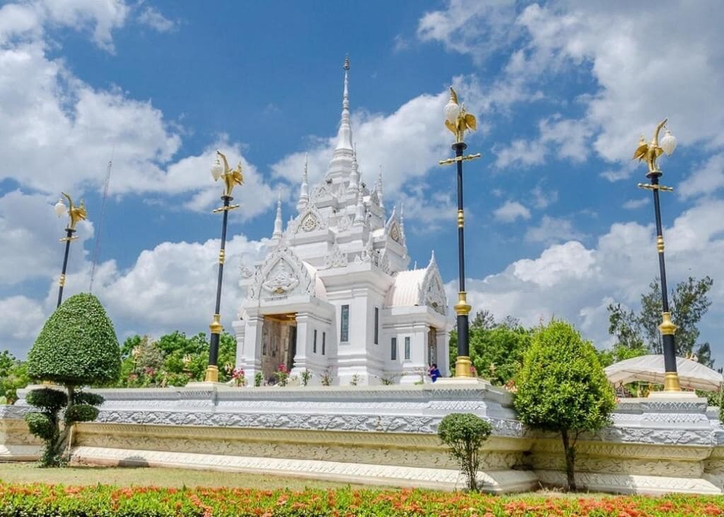 A white temple with a spire, surrounded by a garden with red flowers and trimmed hedges.