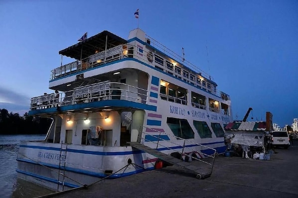 A multi-deck ferry with a name and logo on the side, docked at a pier. - The Port Hostel By Suwatchai (Surat Thani)