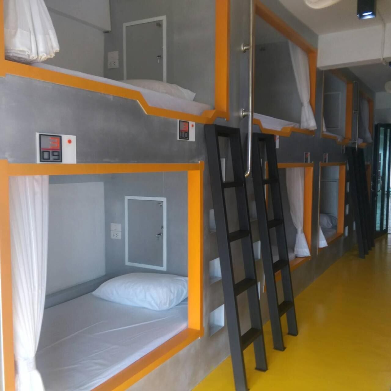 Habitación con literas, un reloj digital, una escalera y una puerta.