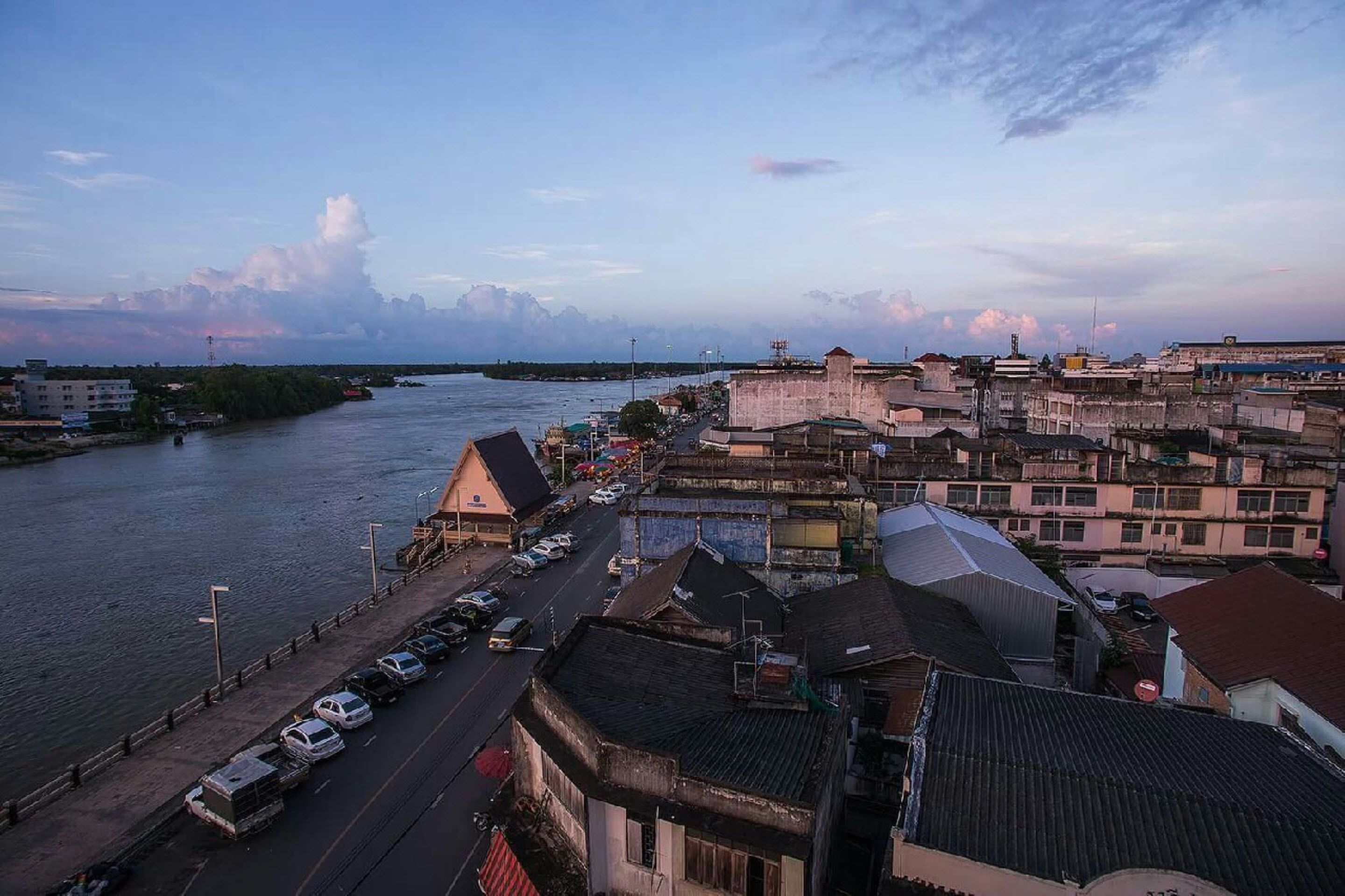 A coastal cityscape with a river, buildings, and parked cars.