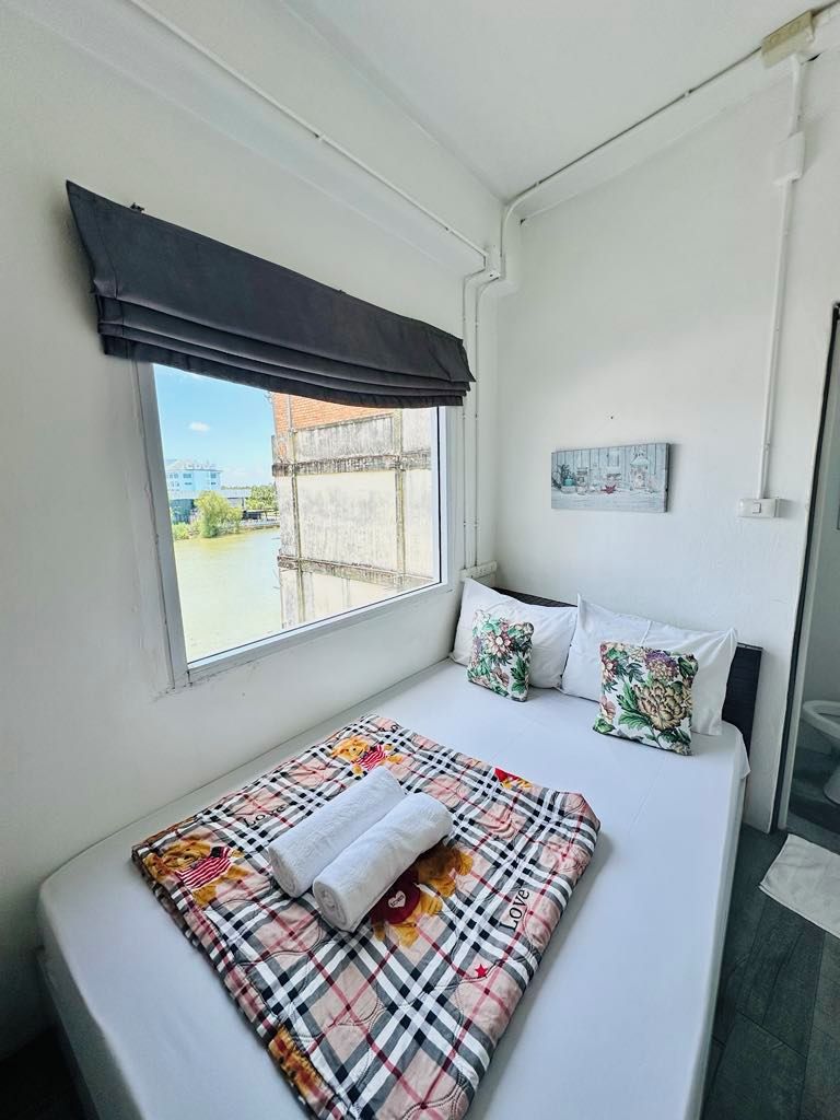 Un dormitorio con una cama grande, una ventana con cortina negra y vistas a un edificio y zonas verdes.