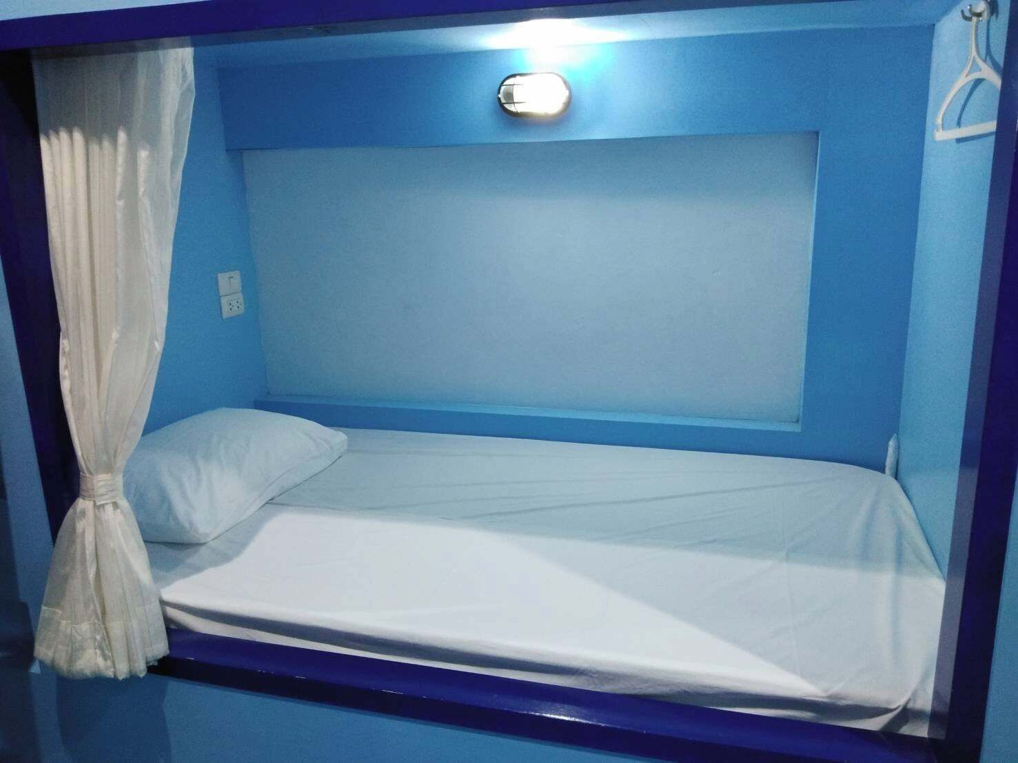 A single bed in a room with blue walls and a white curtain.