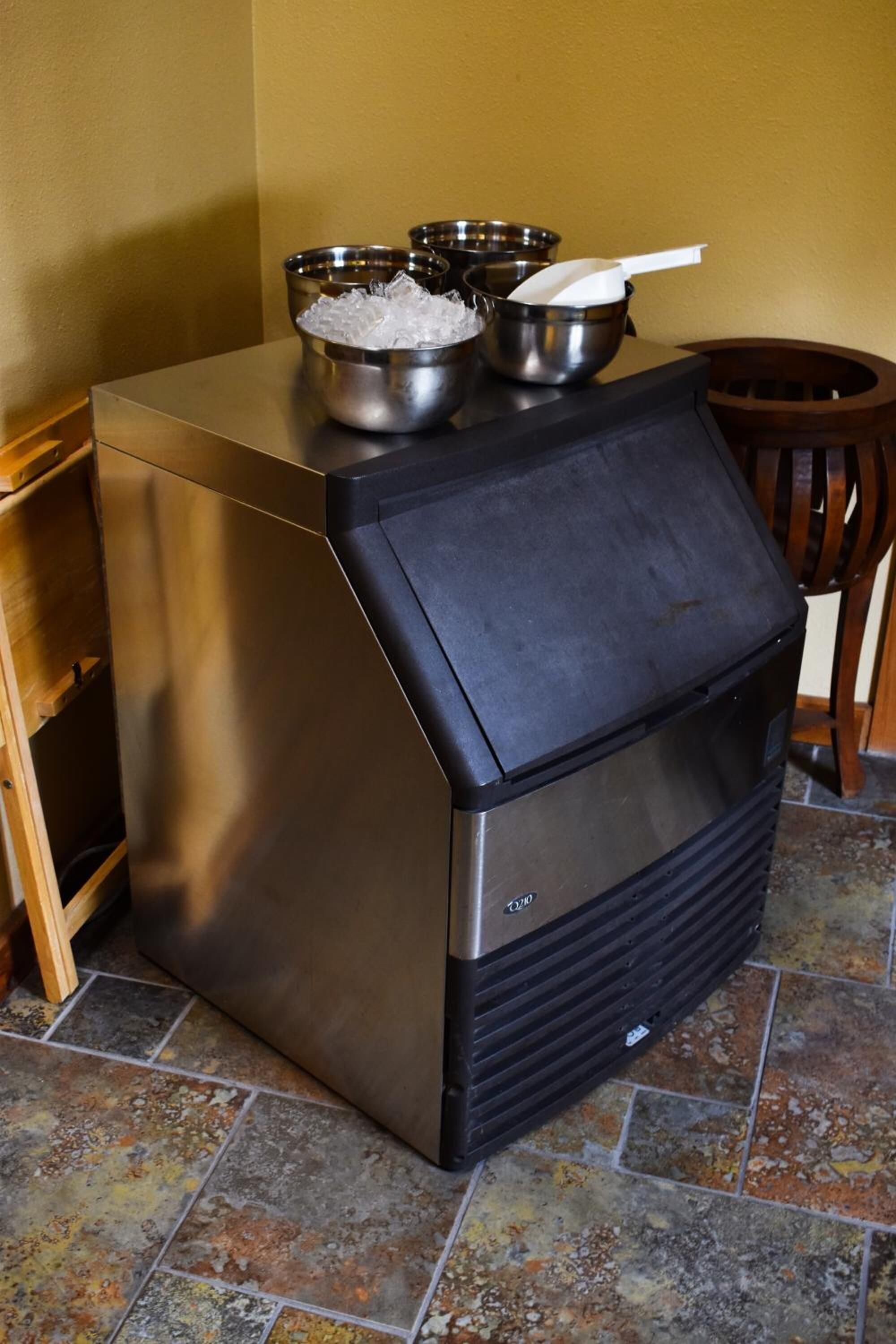 A compact, stainless steel kitchen with a black front panel, a wooden chair, and a tiled floor.