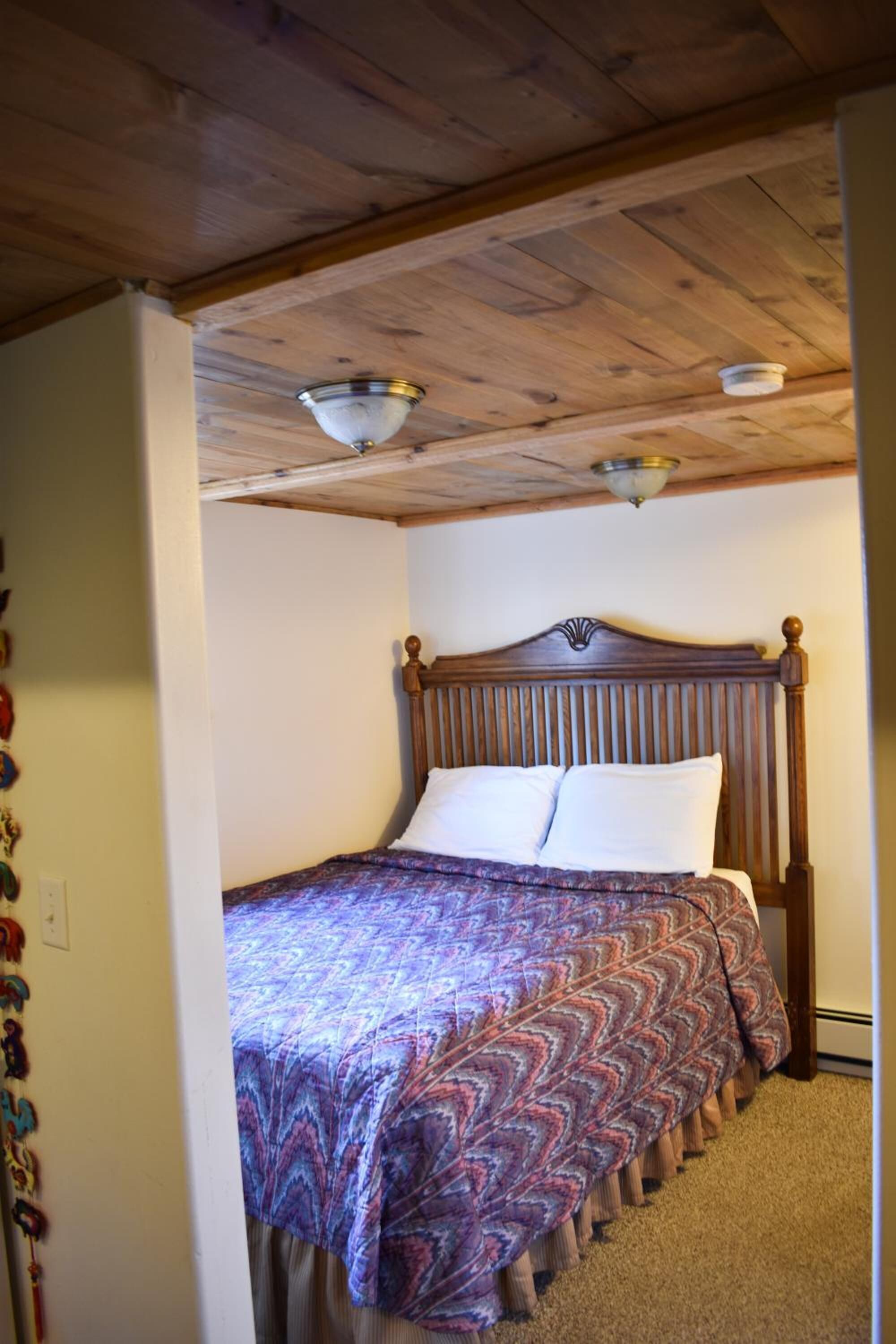 Une chambre avec un plafond en bois, un lit recouvert d’une couvre-lit à motifs et une table de chevet.