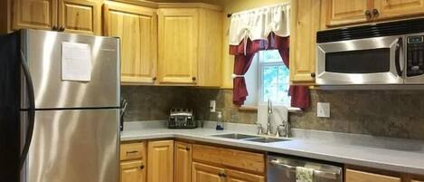A kitchen with wooden cabinets, a stainless steel refrigerator, a microwave, and a dishwasher.