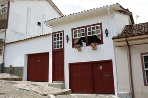 Un edificio blanco con dos puertas rojas, ventanas, un balcón y un techo de tejas.