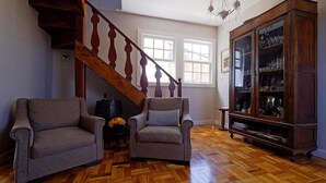 Una sala de estar con dos sillones, un aparador de madera con puertas de cristal, una escalera y una araña.