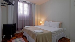 Habitación de hotel con cama, televisor, escritorio y ventana con cortinas.