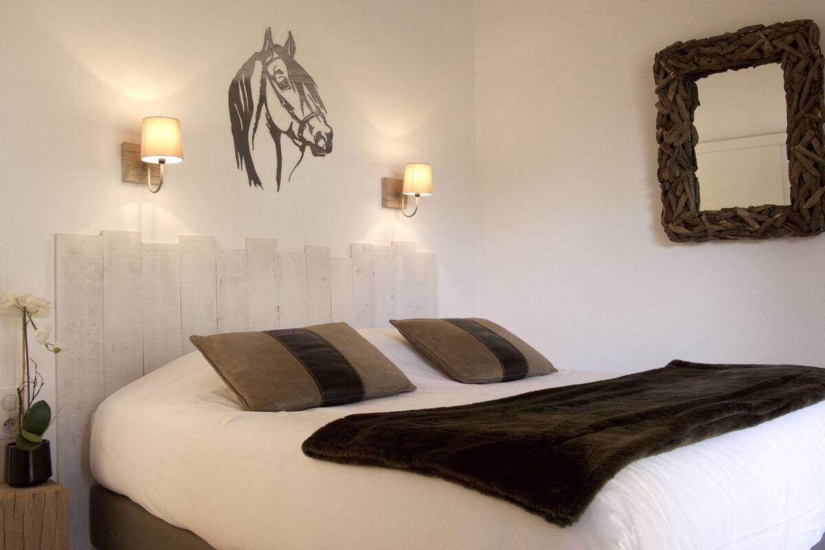 A bedroom with a bed, two pillows, a blanket, a wall-mounted mirror, and two wall sconces.