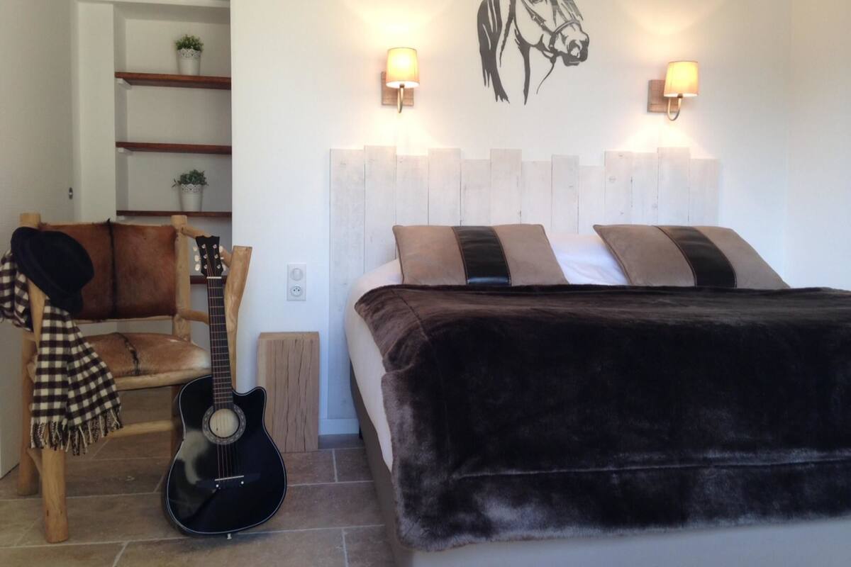 A bedroom with a bed, a guitar, a chair, and a wall-mounted lamp.