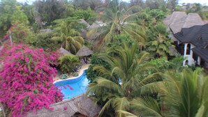 Ein tropisches Resort mit Swimmingpool, umgeben von Palmen und üppiger Vegetation.