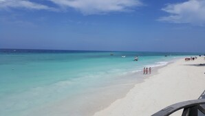 Ein Strand mit klarem türkisblauem Wasser, einem sandigen Ufer und ein paar Booten in der Ferne.