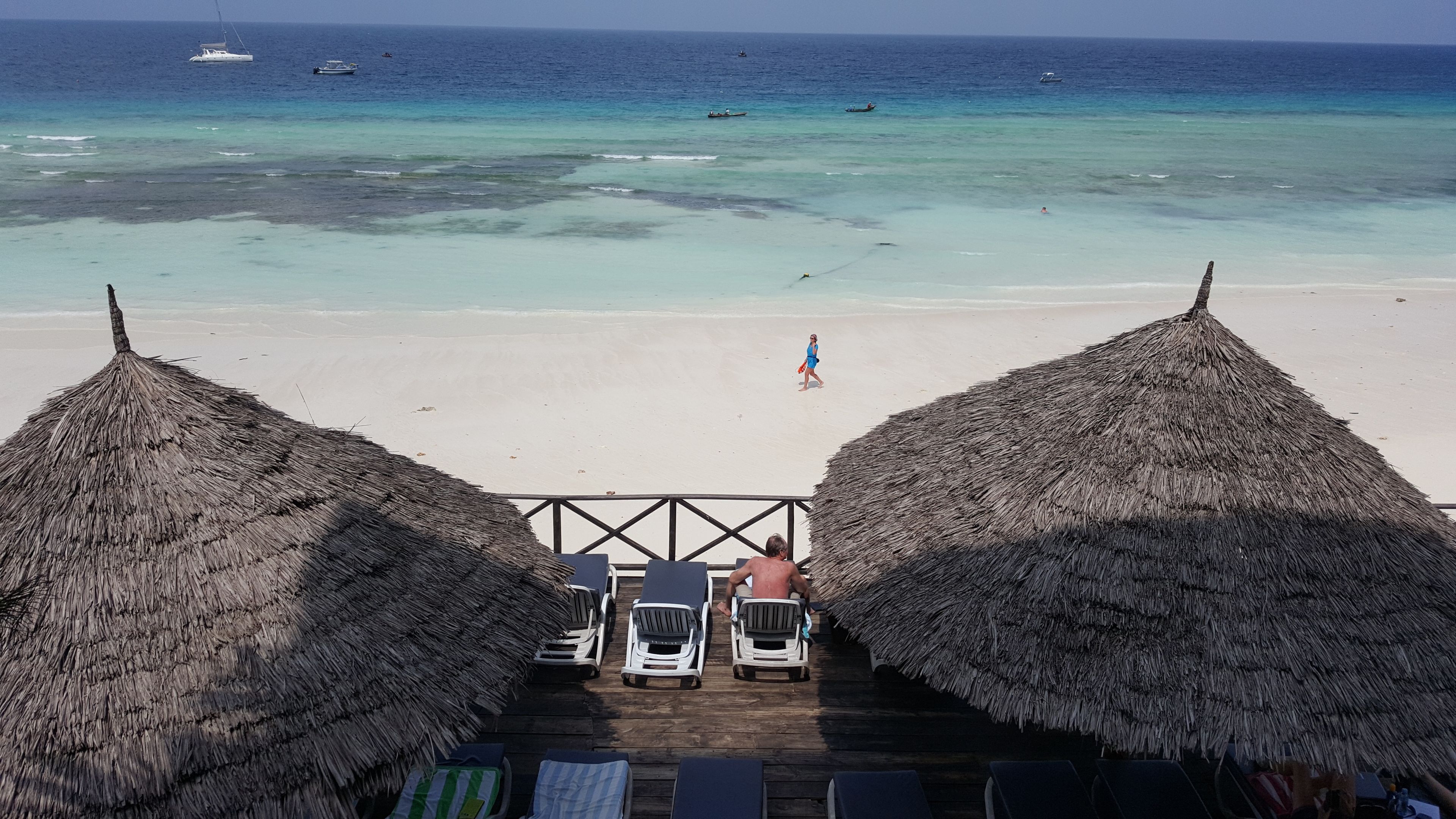 Vista a la playa con estructuras de techo de paja, sillas de descanso y una vista despejada del océano.