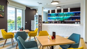 A modern bar area with a white counter, blue and yellow chairs, and a variety of bottles and glasses on shelves. - Osrodek Wypoczynkowy Zorza (Kolobrzeg)