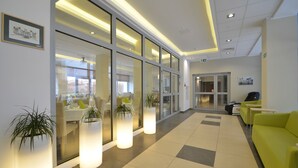 A modern lobby with glass doors, potted plants, and a yellow sofa. - Osrodek Wypoczynkowy Zorza (Kolobrzeg)