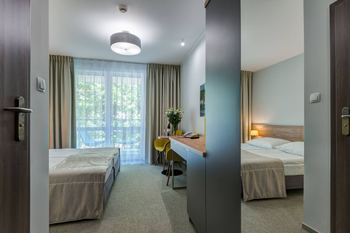 A hotel room with two beds, a desk with a chair, a window with curtains, and a ceiling light.