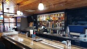 Un espace bar avec un plafond en bois, une variété de bouteilles d’alcool et un comptoir avec des verres et une caisse enregistreuse.