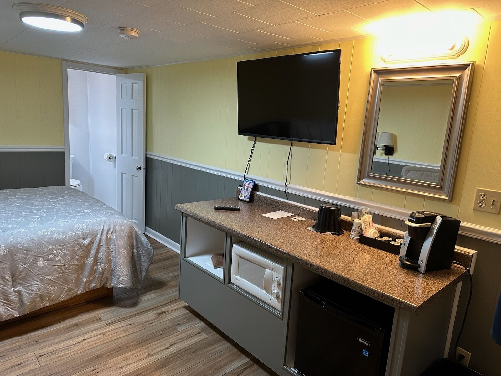 Habitación de hotel con cama, escritorio con cafetera, televisión y refrigerador pequeño.