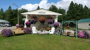 Un bâtiment portant l’inscription « BUREAU », agrémenté de jardinières suspendues, doté d’un espace extérieur aménagé pour s’asseoir et d’une pelouse bien entretenue.