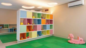 Quarto com uma estante colorida, um tapete de brincadeira verde e um cavalo de brinquedo rosa.
