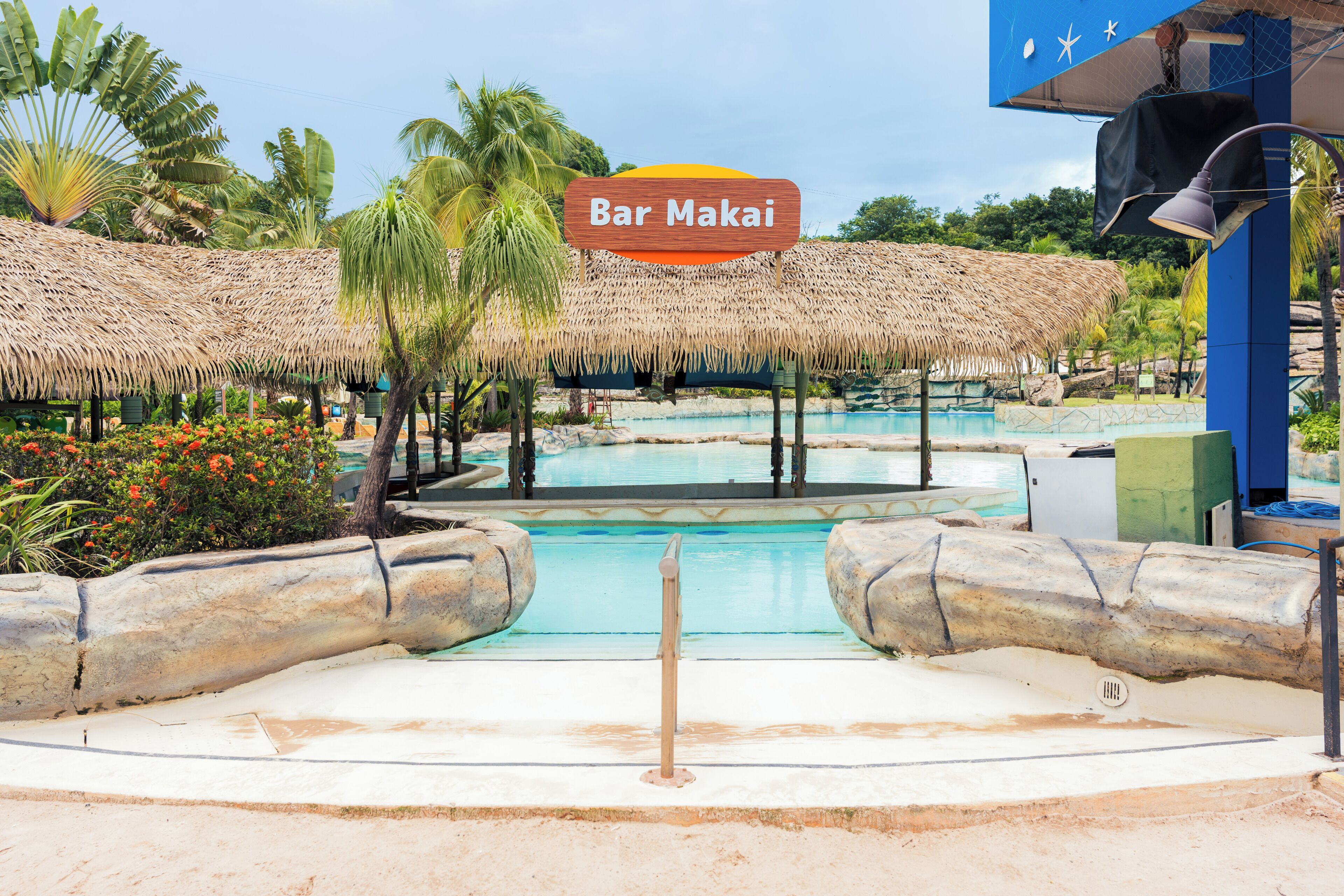 A pool area with a sign reading 'Bar Makai,' surrounded by thatched structures and palm trees.