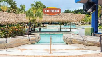 A pool area with a sign reading 'Bar Makai,' surrounded by thatched structures and palm trees.