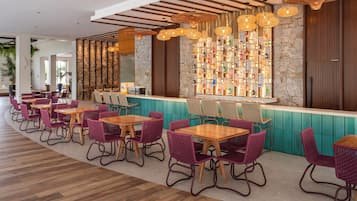 A restaurant with wooden tables and chairs, a stone wall with a bottle display, and hanging wicker lamps.