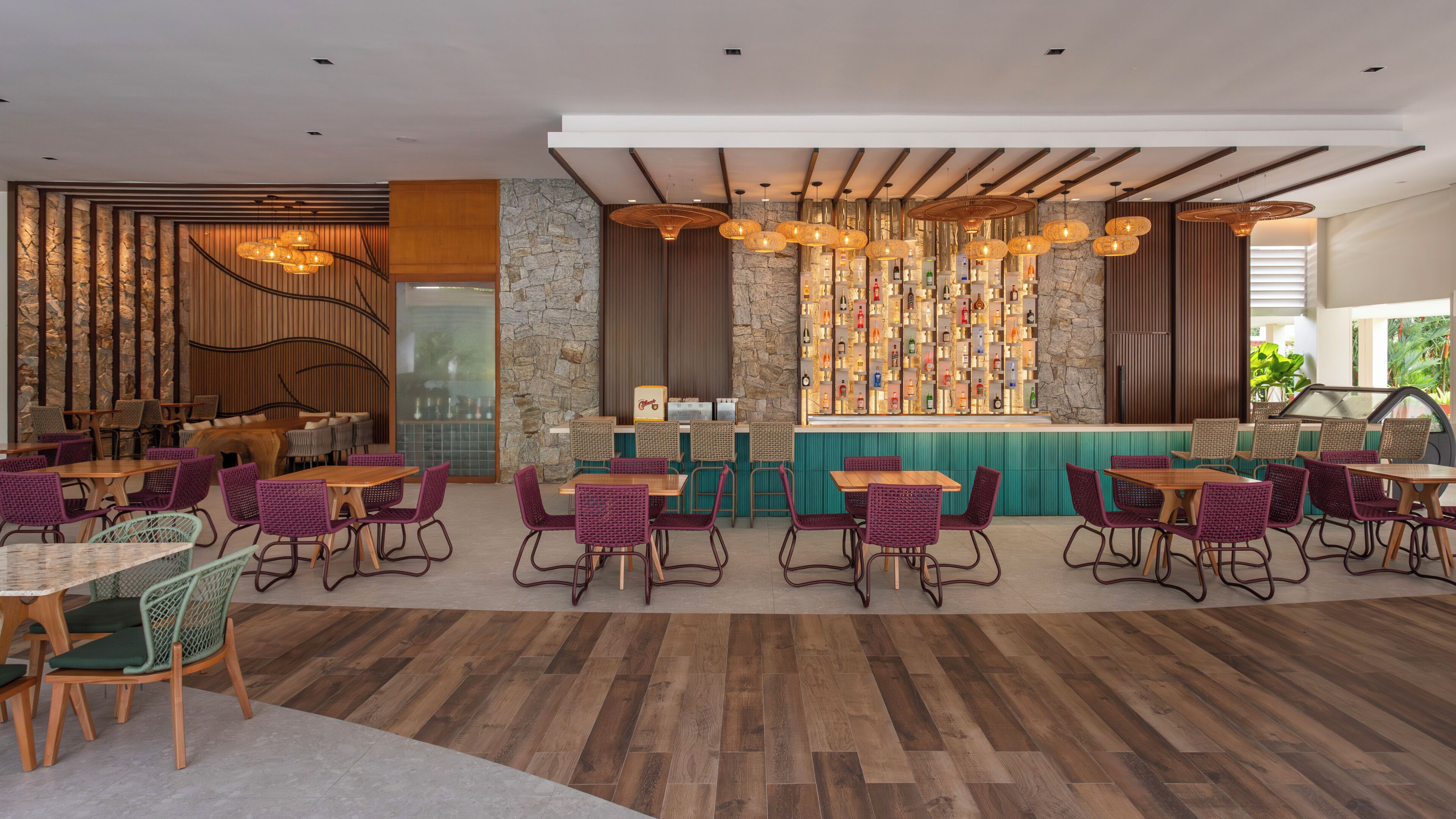Un restaurante moderno con suelo de madera, sillas de mimbre y una zona de bar con un fondo de pared de piedra.