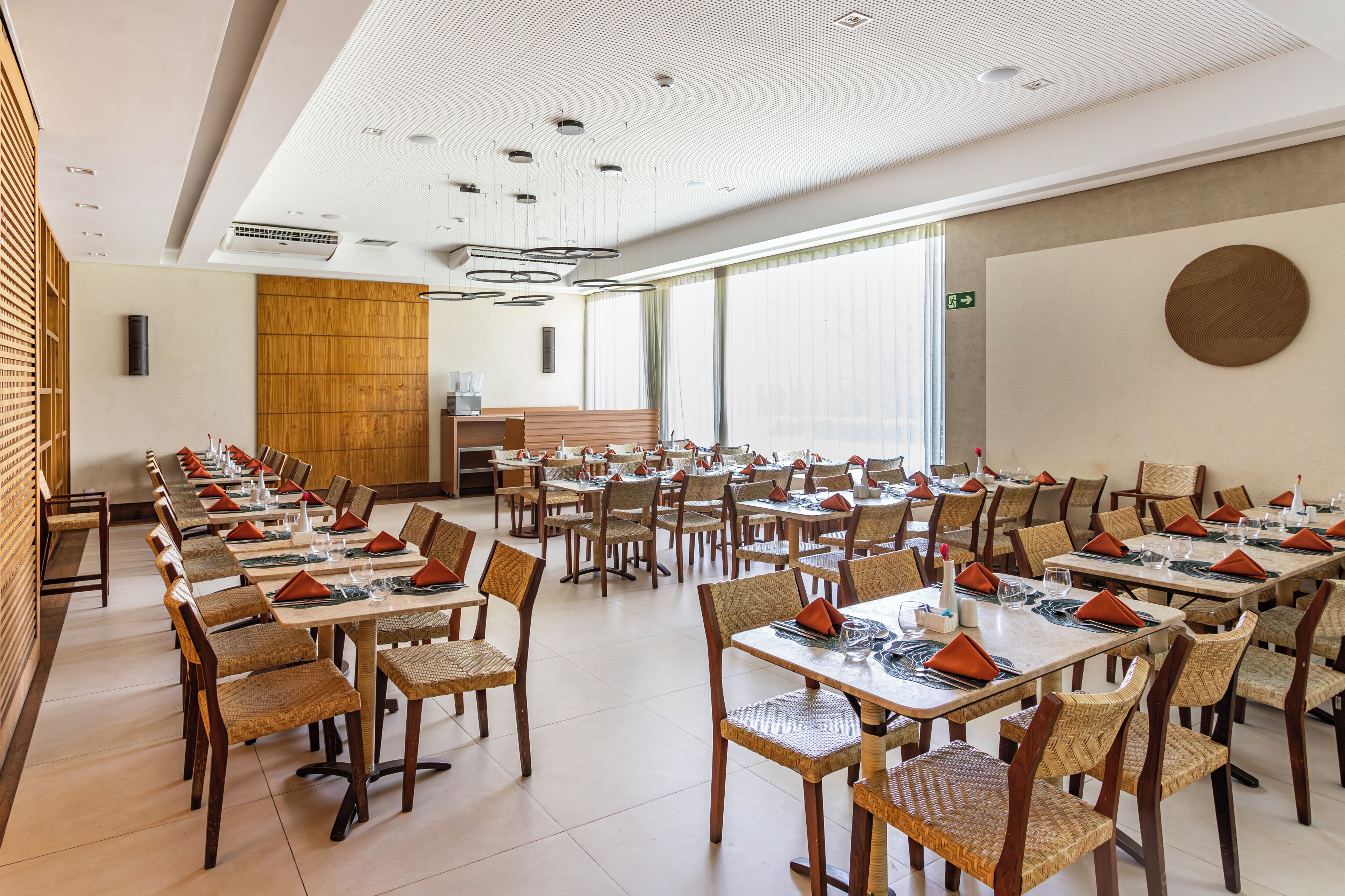 A spacious dining area with multiple tables and chairs, a wooden accent wall, and a large window providing natural light.