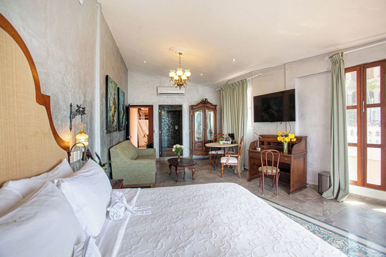 A hotel room with a large bed, a desk, a television, and a dining area.