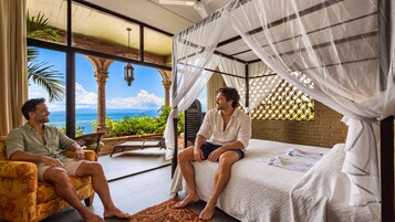 A room with a bed, a bench, and a view of the sea.