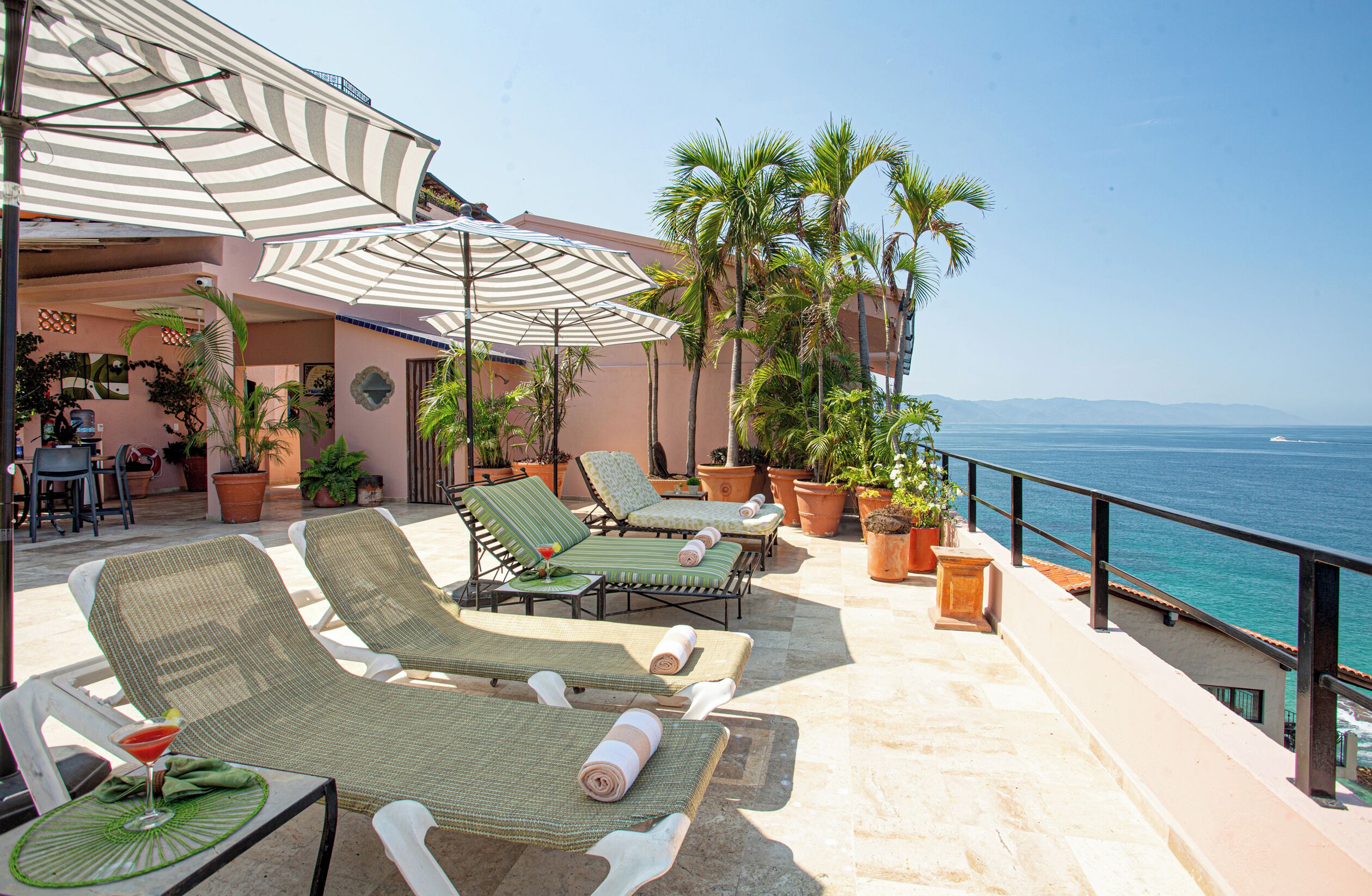 A balcony with lounge chairs, potted plants, and a view of the ocean.
