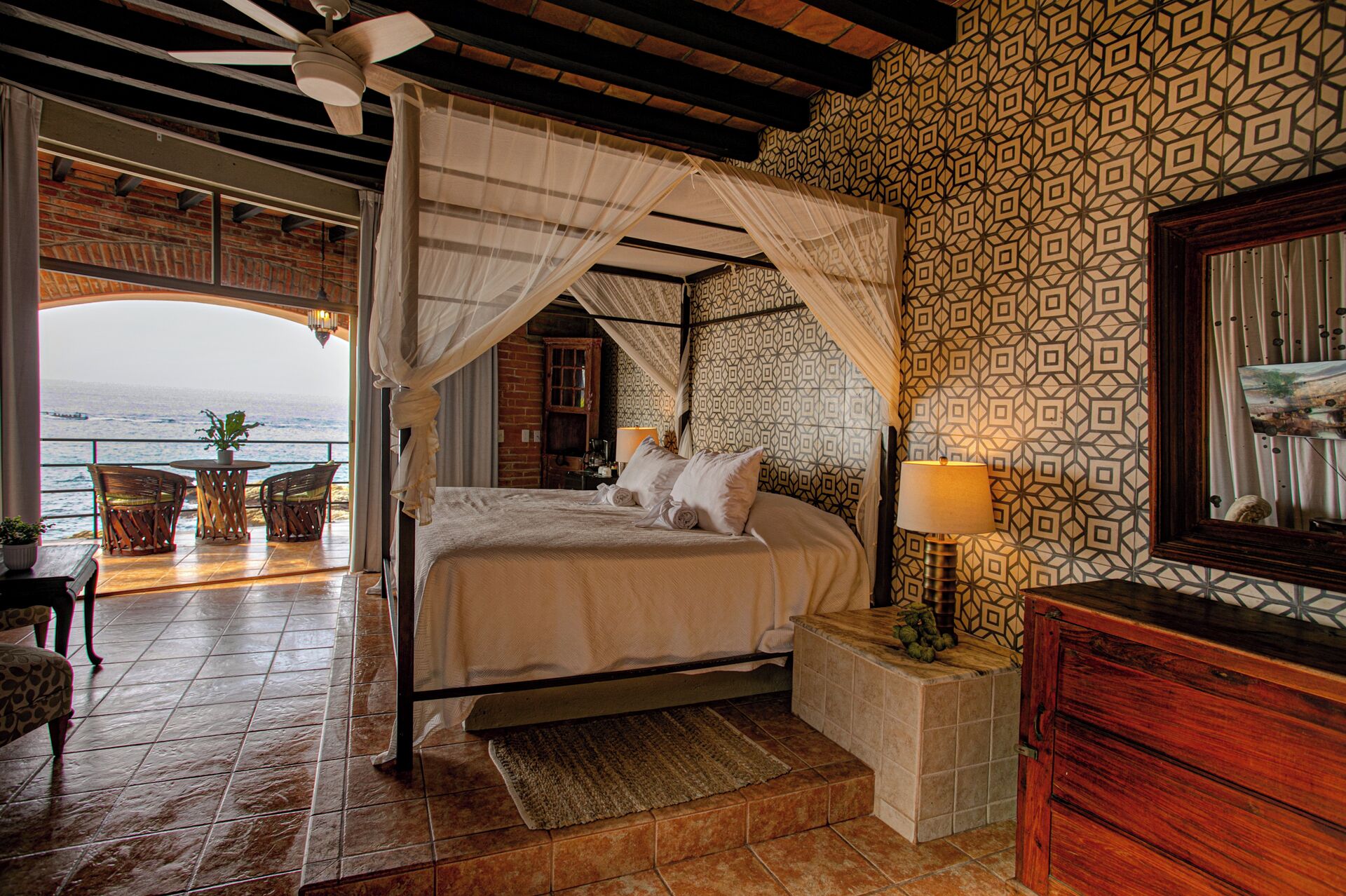 A bedroom with a bed, bedside table, lamp, and a view of the sea.