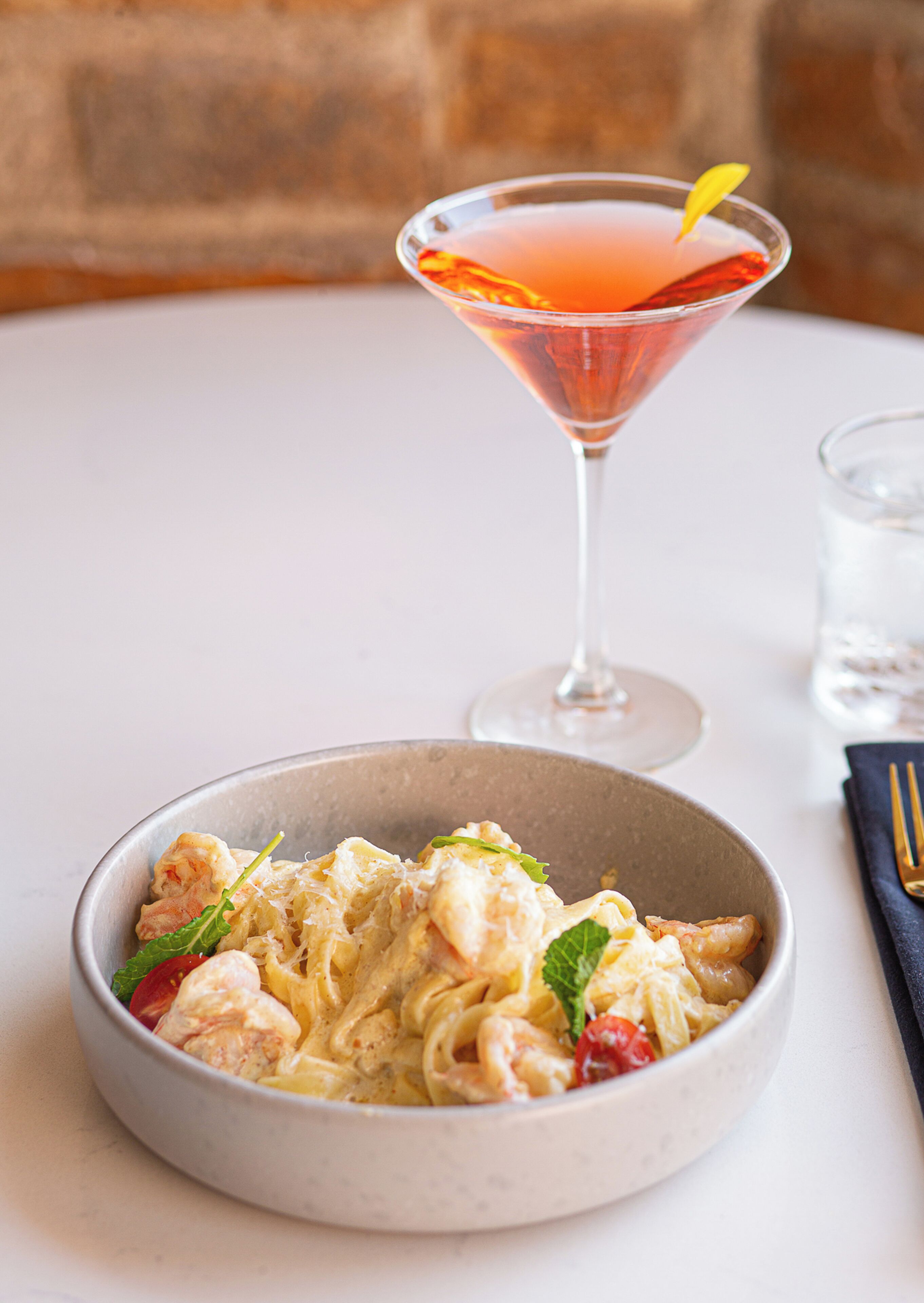 A table with a bowl of pasta and a martini glass.