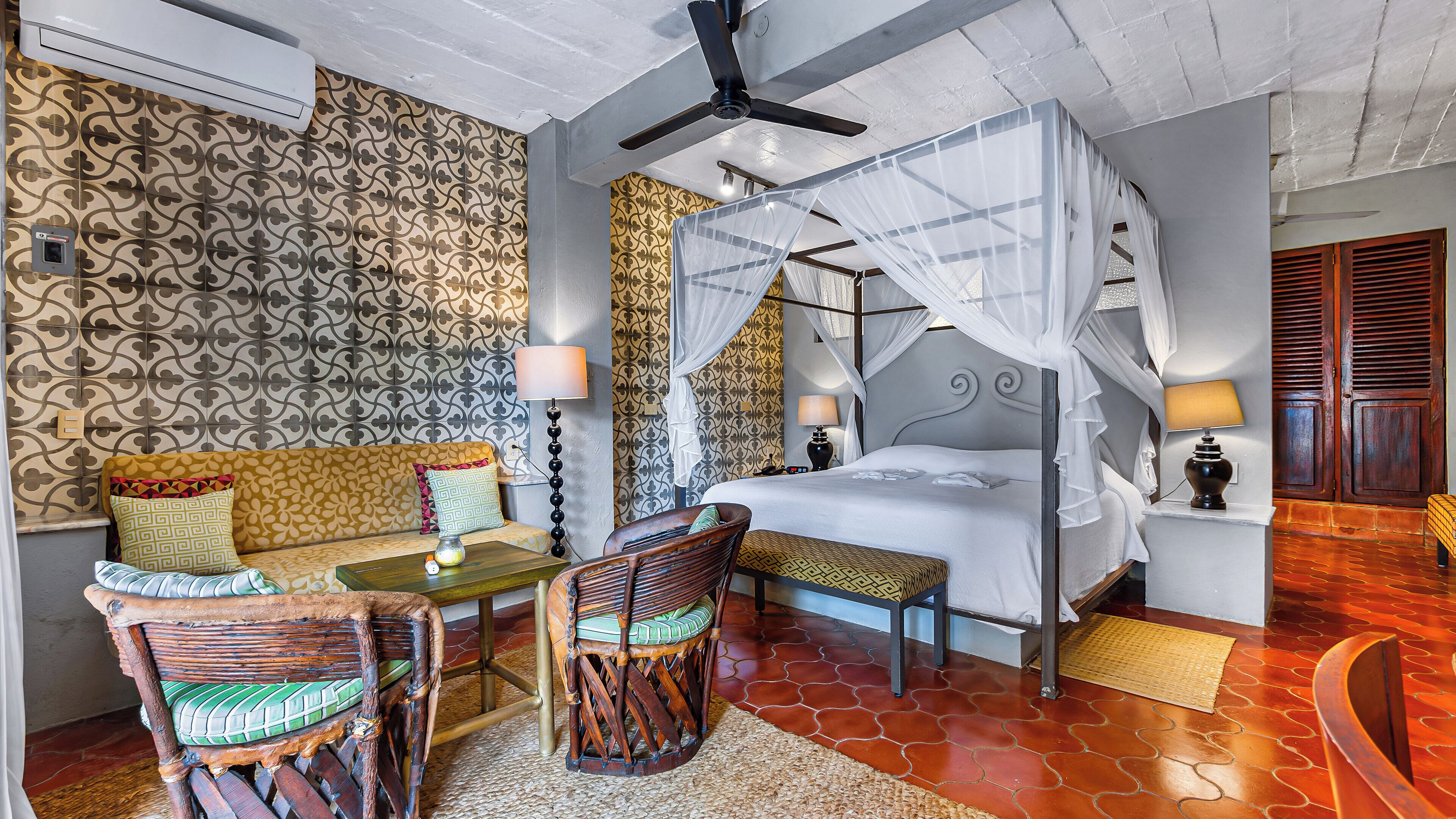 A hotel room with a bed, a sofa, two chairs, a table, a ceiling fan, and a nightstand with lamps.