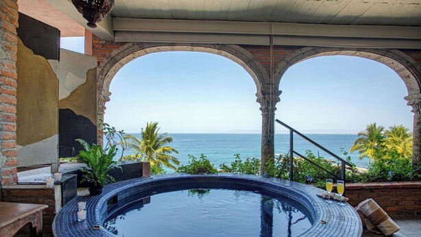Een jacuzzi met uitzicht op de oceaan, een bakstenen muur en een trap naar een balkon.