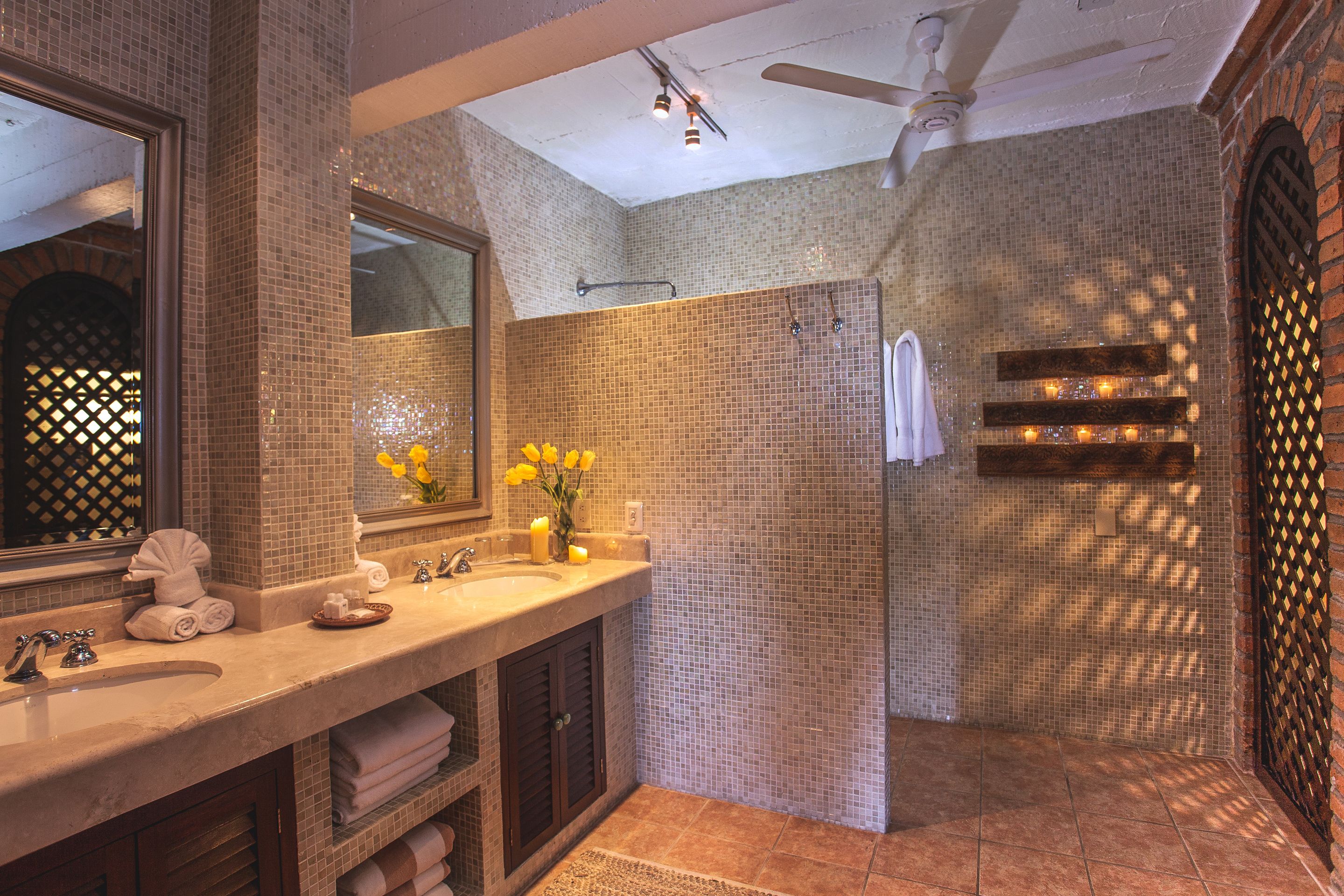 A bathroom with a large mirror, two sinks, a shower, and a ceiling fan.