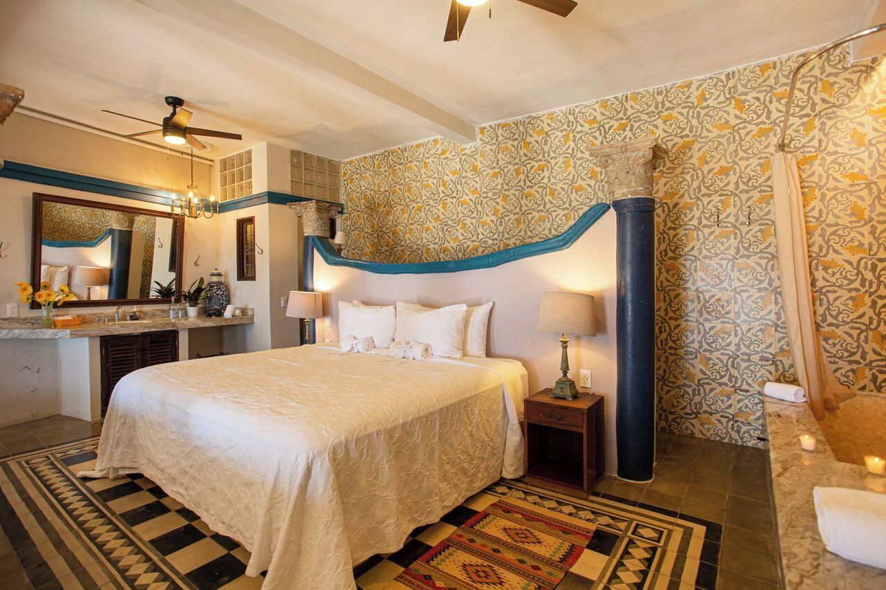 Una camera d'albergo con un letto, una scrivania, uno specchio, cabina doccia e pareti decorate.