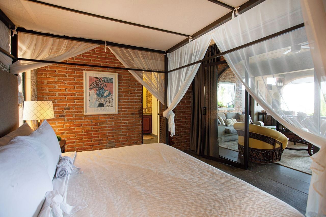 A bedroom with a bed, a window with a view, a brick wall, and a ceiling fan.