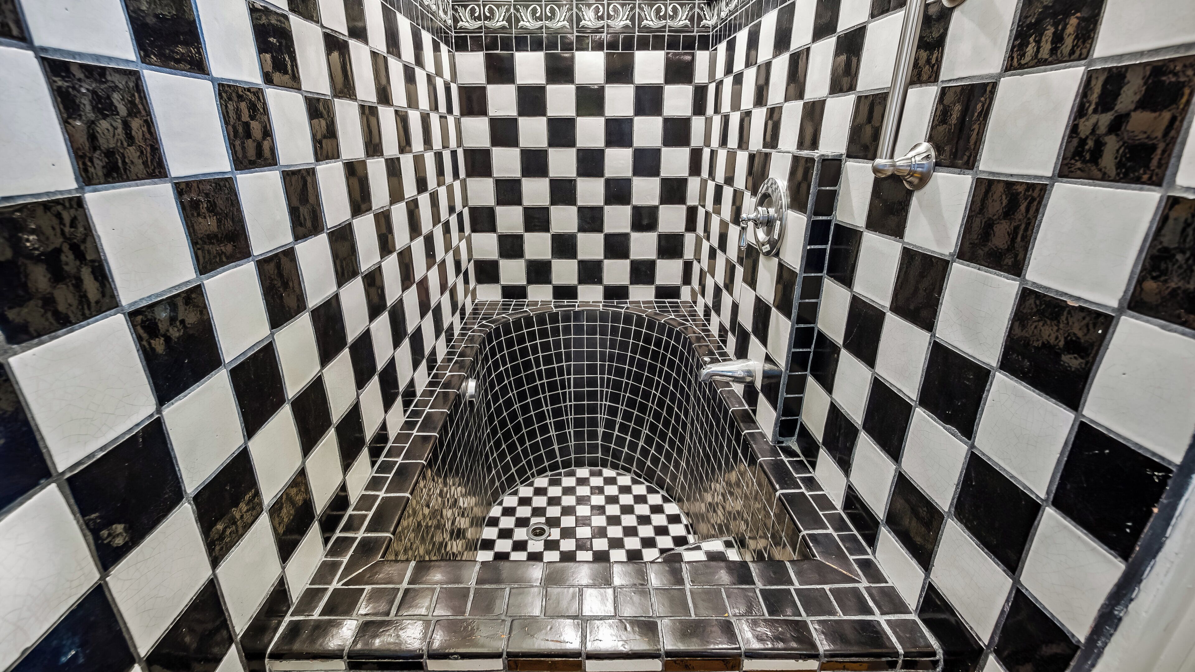 Une salle de bain avec des carreaux noirs et blancs disposés en motif à damier, un drain au centre et un espace douche.