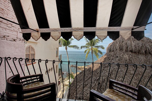 Un balcon avec vue sur l’océan, doté d’un toit de chaume et de deux chaises en bois.