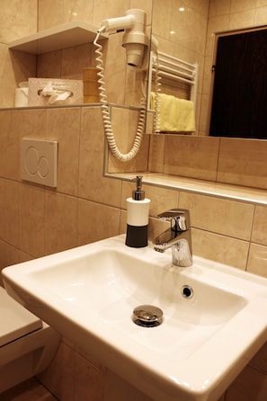 A bathroom with a white sink, a hairdryer, a towel rack, and a mirror. - Hotel Sonnenhof (Maria Rain)