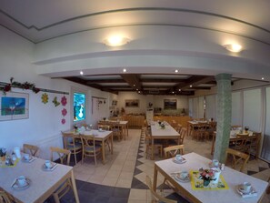 A dining area with multiple tables and chairs, a kitchen in the background, and decorative elements on the walls. - Hotel Sonnenhof (Maria Rain)
