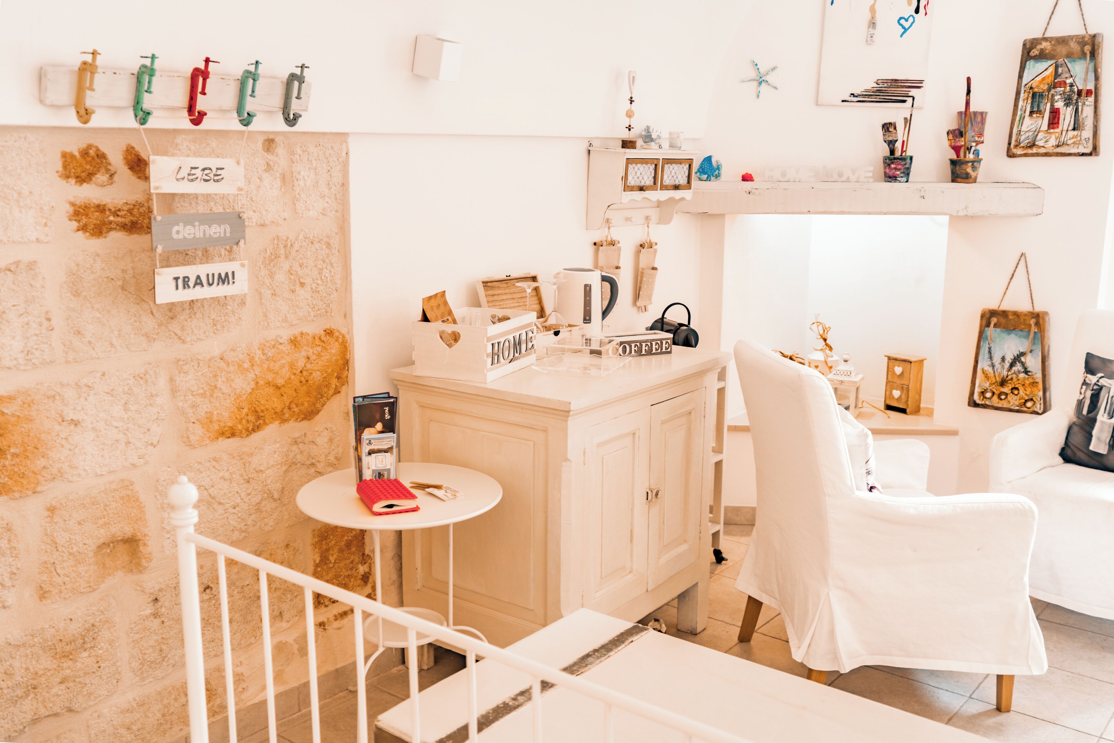 A room with a stone wall, a white cabinet, a small round table, a white chair, and a staircase.