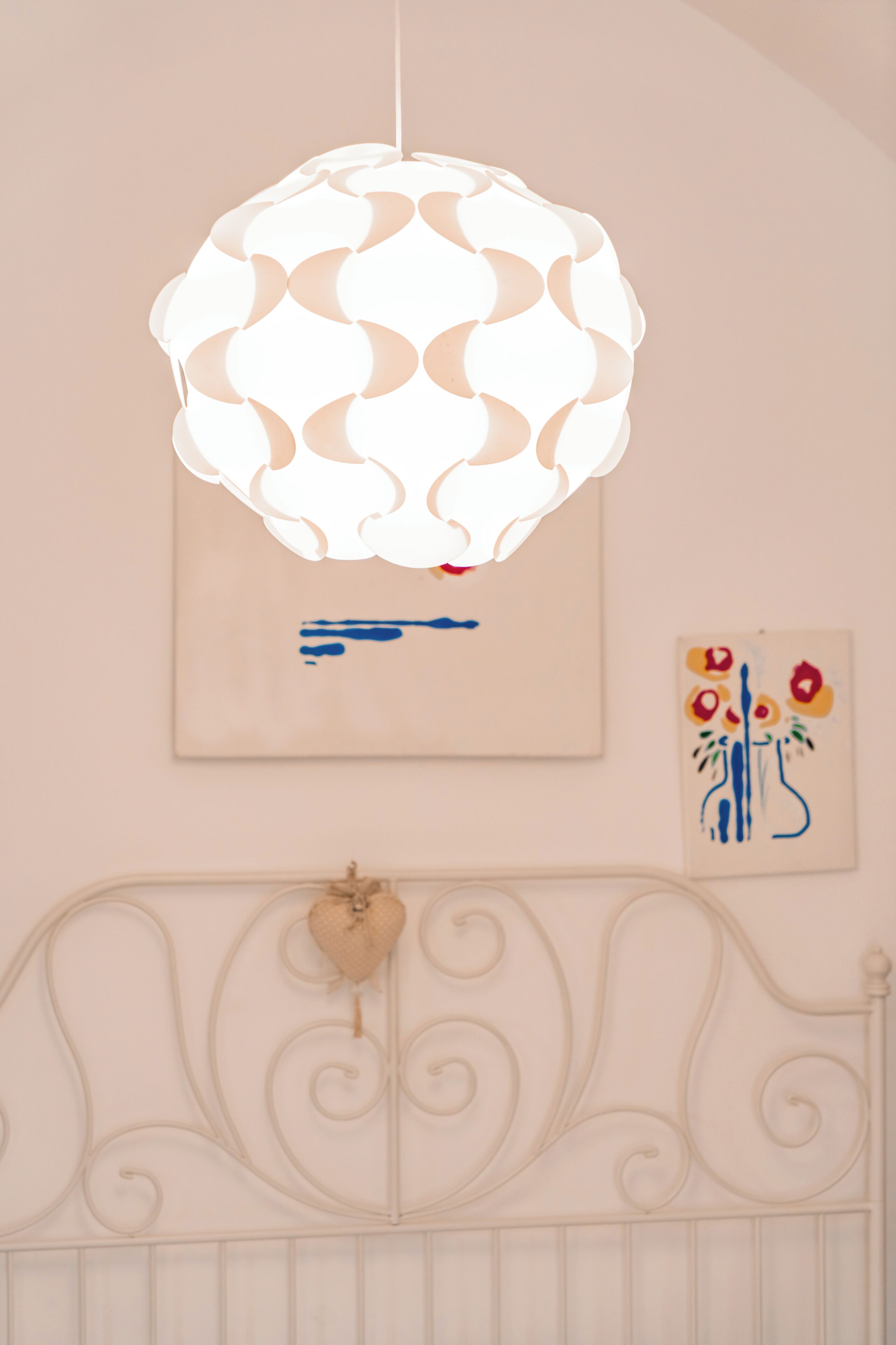 A room with a white ceiling light fixture, a wall-mounted painting, and a decorative headboard.