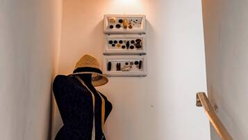 Un escalier avec un mannequin portant une tenue sombre, un luminaire fixé au mur et une étagère contenant divers objets.